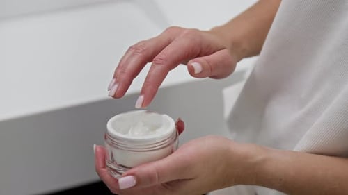 Anonymous Woman Holding Cosmetic Jar and Applying Hydrating Cream to Hand
