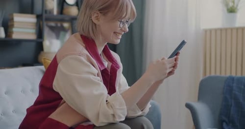 Smiling Woman Using Smartphone on Couch at Home