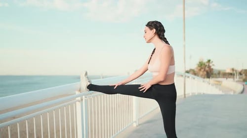 Young athletic woman stretches her body after running on the sea background
