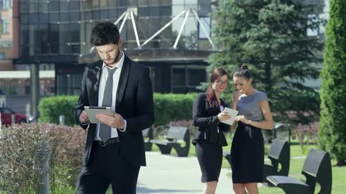 Successful Businessman with Tablet Stands on the Background of Two Businesswomen