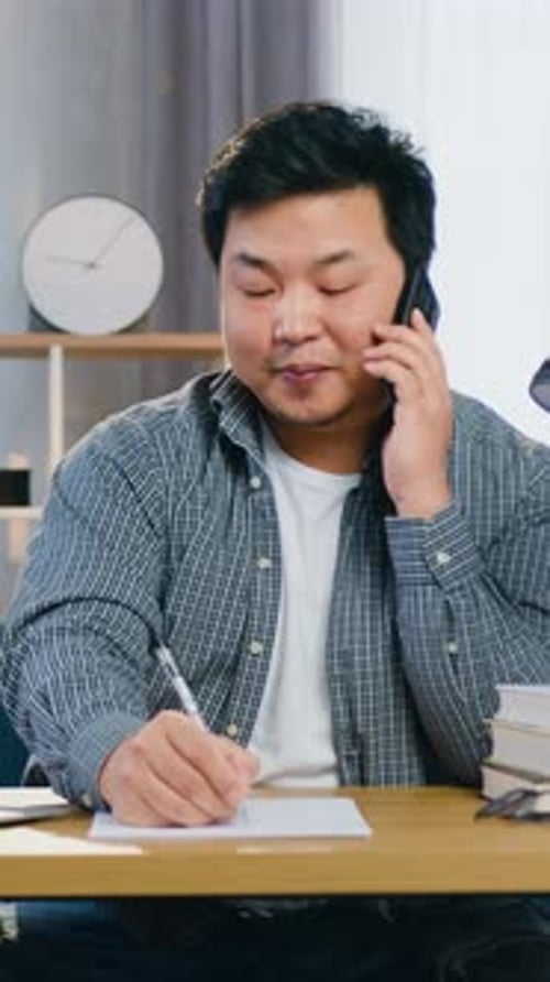Man Talking on Phone, Taking Notes at Desk