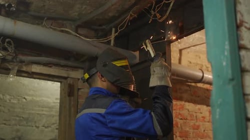 Close Up Side Shot of Professional Welder in Safety Suit and Protective Mask Welds Metal Door Using