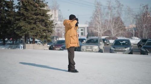 Back View Photographer Capturing Snowy City Cars on Plaza Under Winter Light