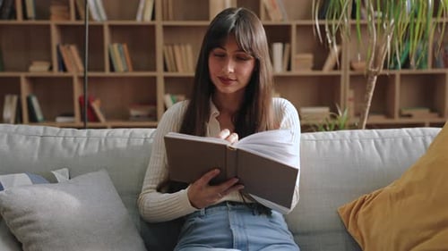 Smiling Gorgeous Caucasian Woman Holding Open Book and Looking Directly Into Camera While Sitting on