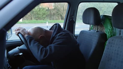 A mature man crying in his car at the side of the road with his head in his hands on the steering wh