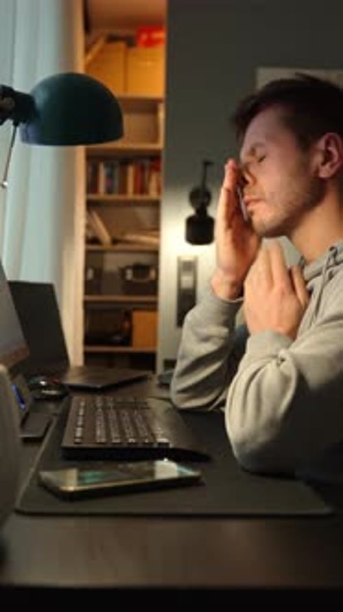 Tired Man Rubbing Eyes During Remote Work with Headphones Fatigued Freelancer