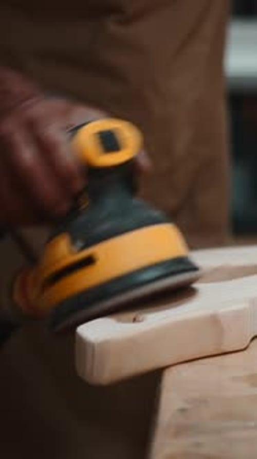 Professional Carpenter Sanding a Wooden Plank with an Orbital Sander in His Workshop