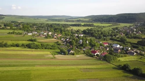Aerial View of Small Village with Small Houses Among Green Trees with Farm Fields and Distant Forest