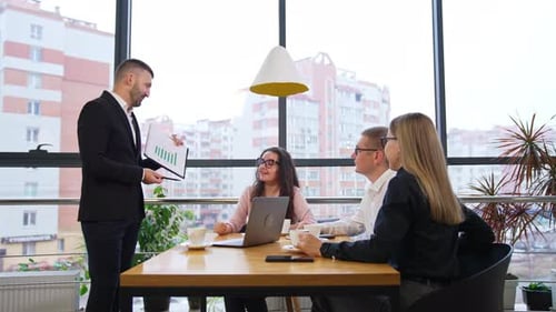 Office team sitting at desk and listen to their chief. Boss shows the chart, asks questions