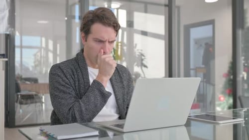 Coughing Young Man Using Laptop in Office