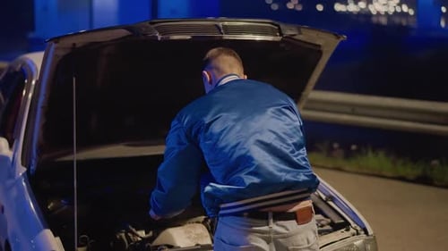 Driver Inspects Engine in Darkness Young Driver Examines Engine Under City Lights Nighttime Roadside