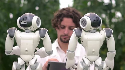Technicien de laboratoire en blouse blanche tenant une tablette et analysant deux robots humanoïdes dans un vert