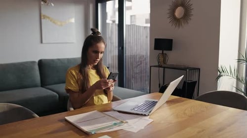 Woman works at laptop and uses phone