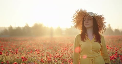 Brunette Woman in a Yellow Dress and Straw Hat in Poppy Field at Sunrise