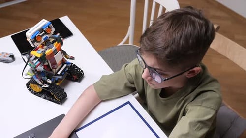 Young Boy with Glasses Focused on a Laptop Screen Learning Coding and Robotics While Building an
