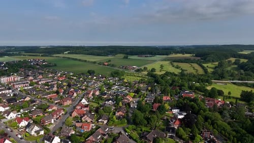 Small american city with rural countryside fields on hill during sunny day in June. Aerial lateral w