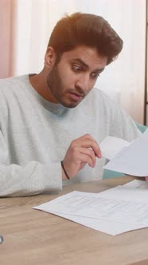 Concerned Man Reviews Documents at Desk Indoors