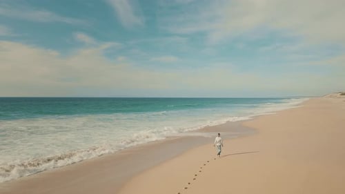 Woman walking barefoot by the sandy beach, leaving footprints in the sand. She is enjoying summer.