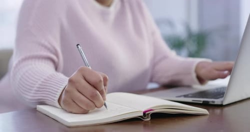 Séquence vidéo 4k d'une femme méconnaissable prenant des notes tout en utilisant son ordinateur portable