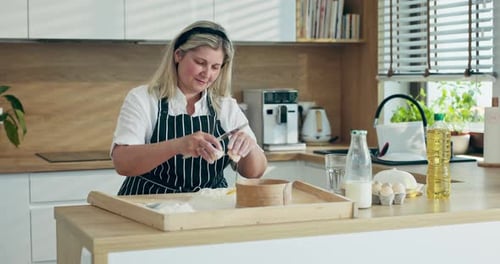 Blonde Woman Cracking Eggs in Bright Kitchen