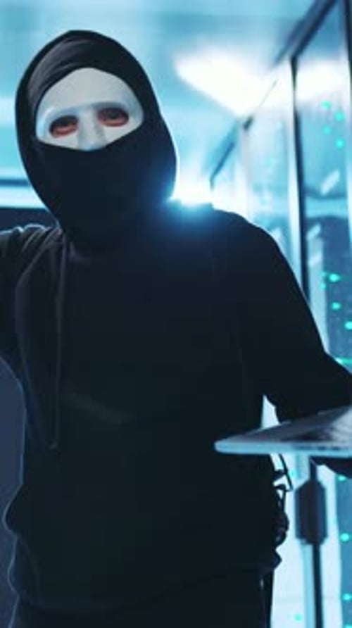 Anonymous masked person using laptop in server room