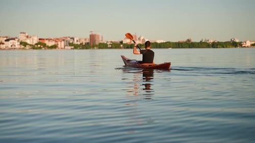 Kayaker Paddling on Calm Lake with City Skyline