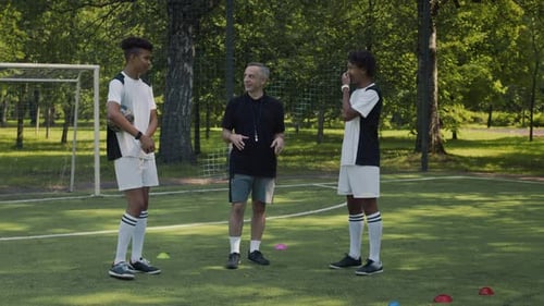 Soccer Coach with Two Team Members Talking on Grassy Field during Training