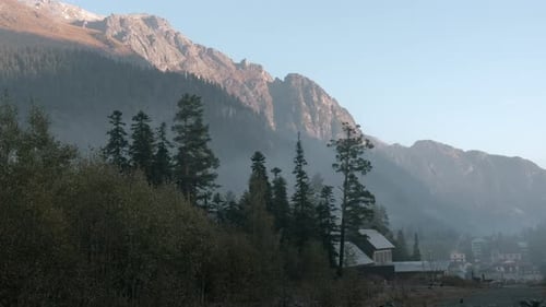 Village in mountains with dense forest and moving fog on background of rocks