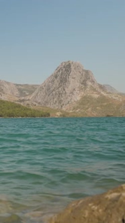 Vertical video. Crystal Clear Lake with Rocky Shores, Majestic Mountains in the Background, Captured