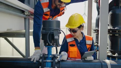 Two professional industrial engineers inspect a large pipe valve at a manufacturing plant.