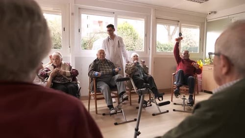 Friendly Caregivers Assisting Senior People in Pedal Exercise and Weightlifting at Nursing Home