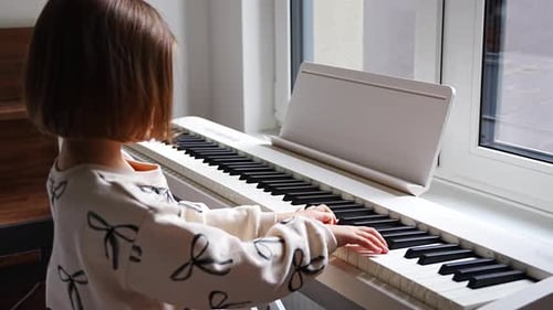 Child Plays Piano by Window in Home