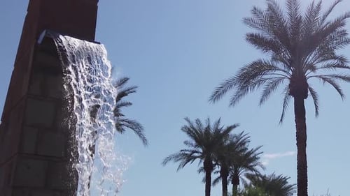 Slow-motion tilt-down from the spout of a freestanding water feature, a brick fountain surrounded by