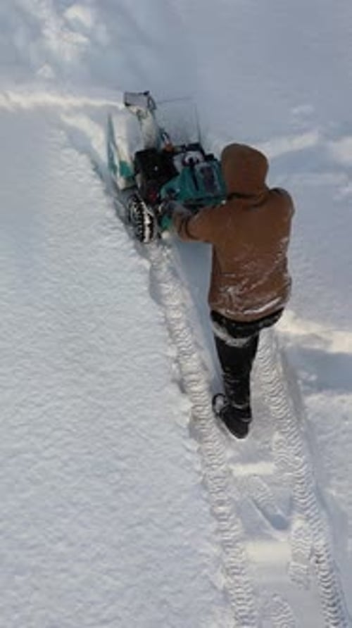 Vertical Man Dressed in Winter Clothes Moves Snow Blower Forward