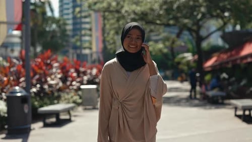 Adult Lady Wearing Hijab Outside Walking on the Street While Speaking on the Telephone