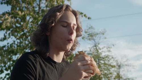 Young Adult Eating Sandwich Outdoors on Sunny Day