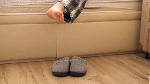 Personne mettant des pantoufles en sortant du lit en pyjama