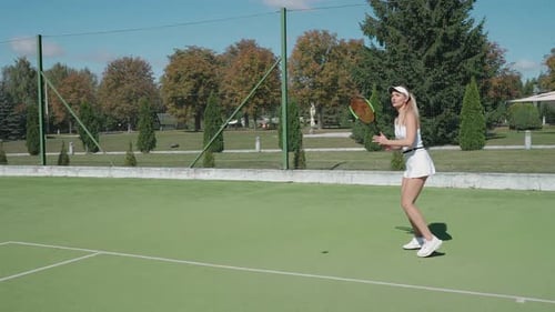 Woman Practices Tennis on Outdoor Court on Sunny Day