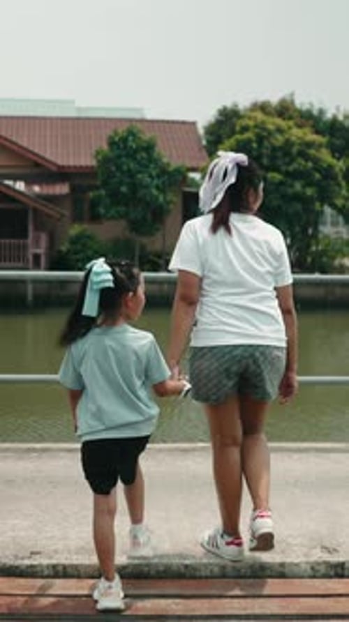 Mother Walking with Child Along Riverside Sharing Peaceful Moment in Green Natural Setting