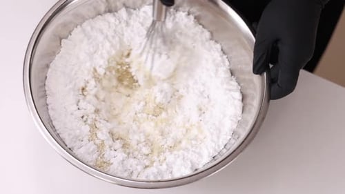 White flour in a steel bowl close up. Confectioner hands in black gloves stirs dry ingredients