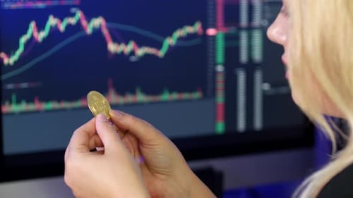 Woman Holding Bitcoin Coin in Front of Computer