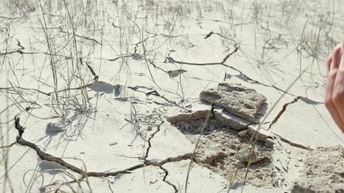 Hand Breaking Cracked Earth in Arid Landscape