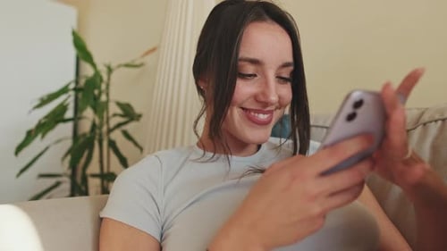 Close-up of smiling young woman using phone while sitting on sofa at home