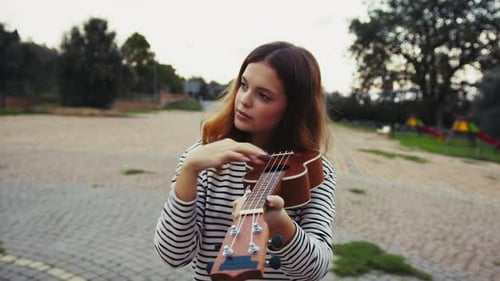 Girl Plays Ukulele As If It Were A Violin Musical Instrument In The Park