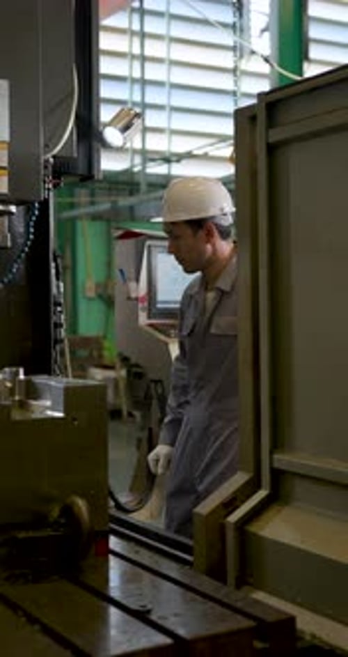 asian adult male engineer reaches into CNC machine area during slow motion inspection, checks