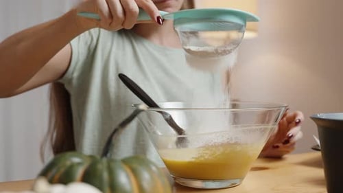 Woman is making pumpkin cookies, she sifts flour into a bowl with pumpkin puree. In slow motion.