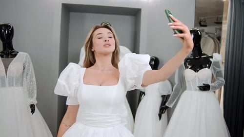 Retrato de noiva loira fazendo selfie fotográfica usando smartphone enquanto experimenta o vestido no salão de casamento