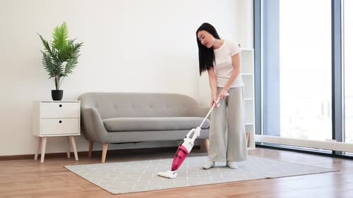 Woman vacuums rug in well-lit apartment