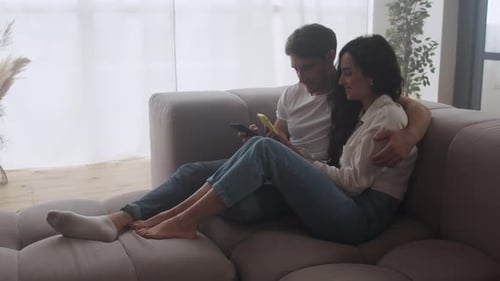 Affectionate couple relaxing on couch looking at phones