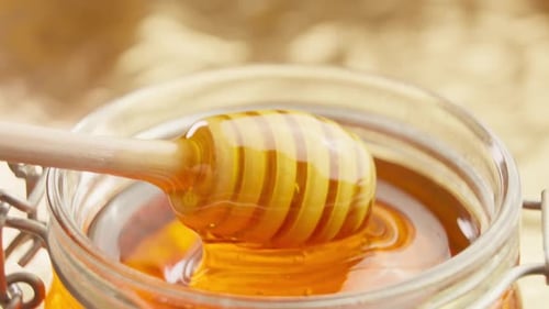 Golden Honey Drizzling from Dipper into Glass Jar
